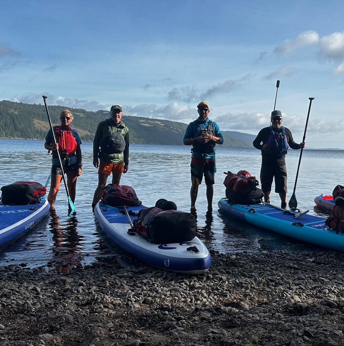 Paddlers with loaded boards beside a scenic lake