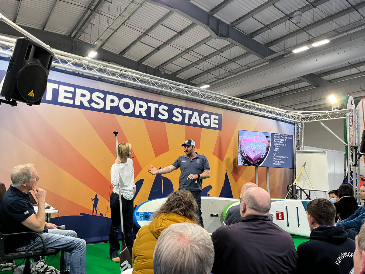 Brendon Prince demonstrating paddleboarding technique on a watersports stage in front of an audience